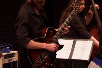 Three musicians, pianist in foreground, guitarist in the middle, cellist in the background.