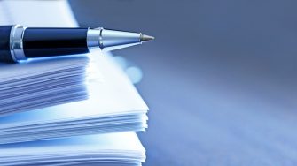 A ballpoint pen rests on top of a stack of documents ready for signing.  The image is photographed using a very shallow depth of field with the focus being on the tip of the pen.