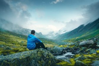 man sitting on rock with mountainous view