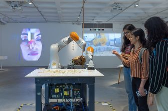 Three students interact with a robot arm, sweeping small object.s