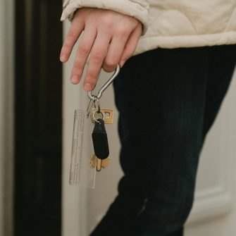 Close crop image of a hand holding a pair of housekeys, walking through an indoor space.