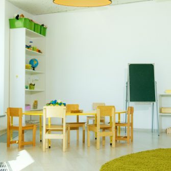 An empty white daycare room with small table and chairs, bookshelves and a blackboard