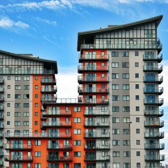 Two grey and orange apartment buildings stand against a blue and cloudy sky