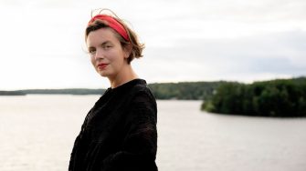 Researcher Bronwyn stands in front of a calm body of water with a bright red headband a highlight among muted tones of land and water