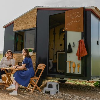 A couple sits outside a black tiny house