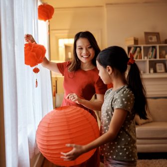 Happy Chinese mother and daughter decorate home with red lanterns for Lunar New Year
