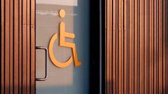 Accessible wheelchair restroom sign on glass sliding door with wooden wall in public area
