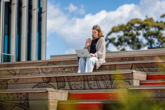 Student waving at laptop while sitting on stairs.