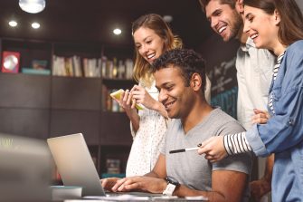 Students surround a laptop, smiling