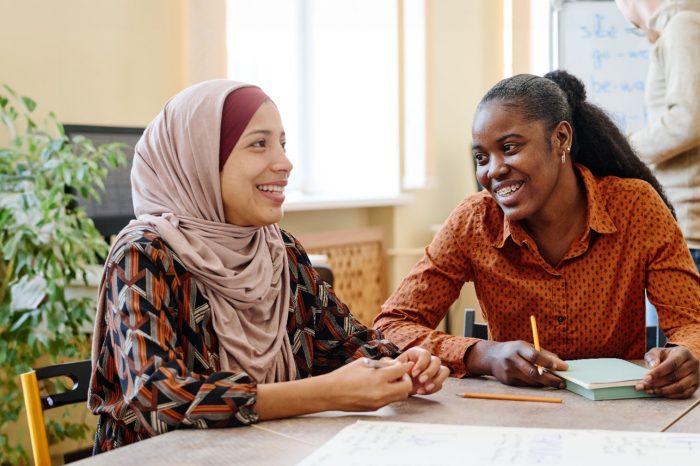 Young Black and Middle Eastern women having fun chatting about something during English lesson for immigrants