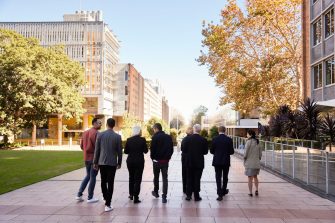 8 UNSW alumni in business attire walk on UNSW Kensington Campus main walkway below on the main steps