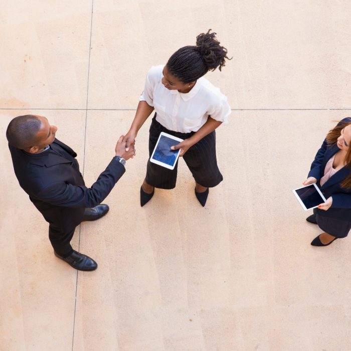 3 business people with iPads talking and shaking hands dressed in business attire