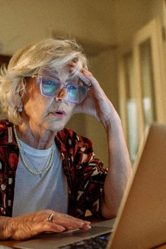 Worried elderly woman looking at laptop while managing finances at night