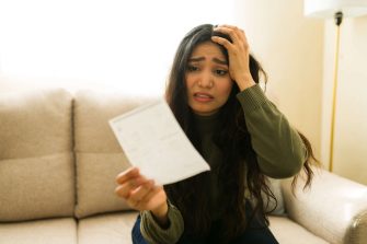 A woman looks distressed while holding a bill at home
