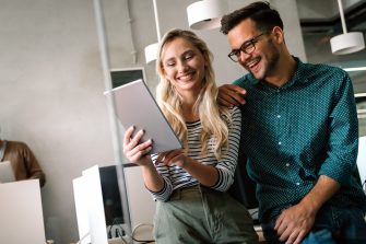 Young manager talking with experienced colleague while using computer in office. Colleagues discuss business, financial and marketing projects. Specialists work in diverse startup team.