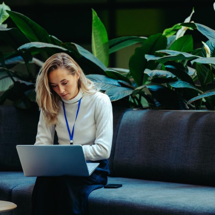 A woman sitting on a sofa, working on her laptop.