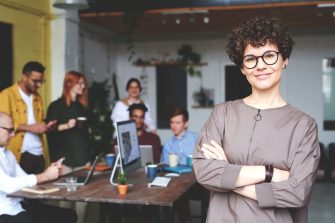 Photo of woman wearing eyeglasses with co-workers in the background