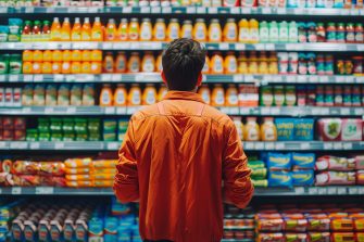 A man standing in a supermarket aisle, intently focused on the shelves. A moment of contemplation and decision-making. Concept of inflation crisis.