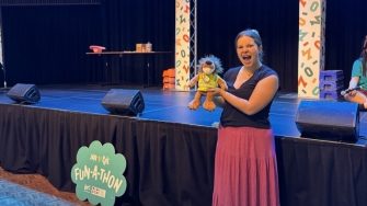 Student posing with a plushie in front of the Fun-a-Thon stage at the Roundhouse