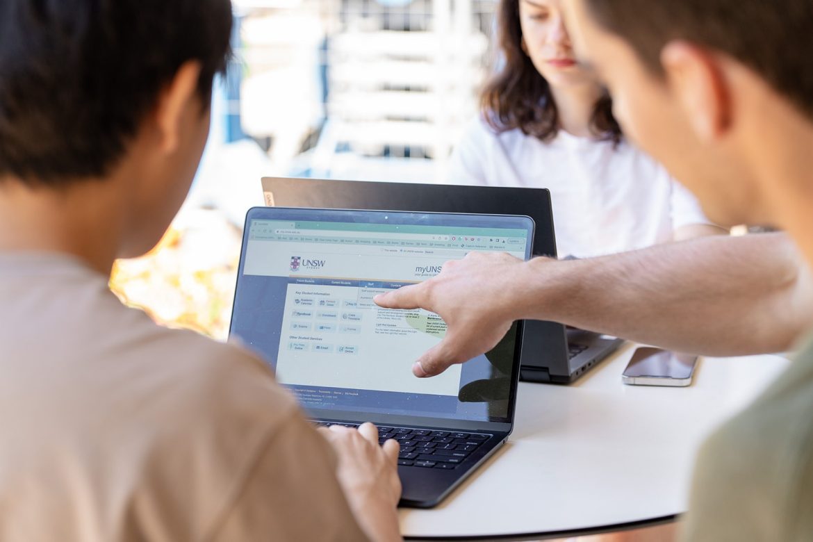 Two students using a laptop at a table beside Library Lawn