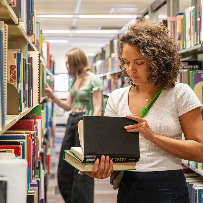 A student looking at a book in an aisle of the library