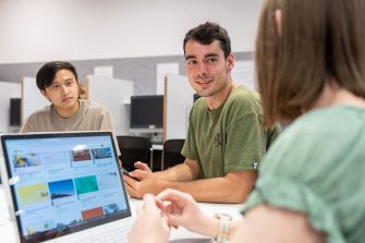 Students using their phones and laptops while sitting around a table