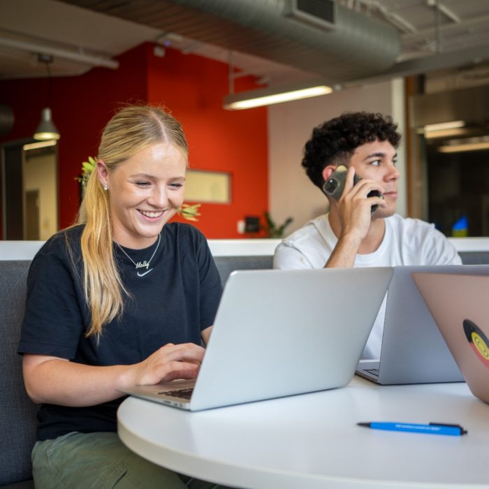 Three students sitting at a table with phones and laptops at Nura Gili on Kensington Campus