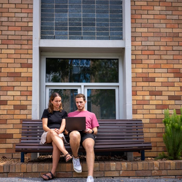 Two students sitting on a bench with a laptop on Kensington Campus