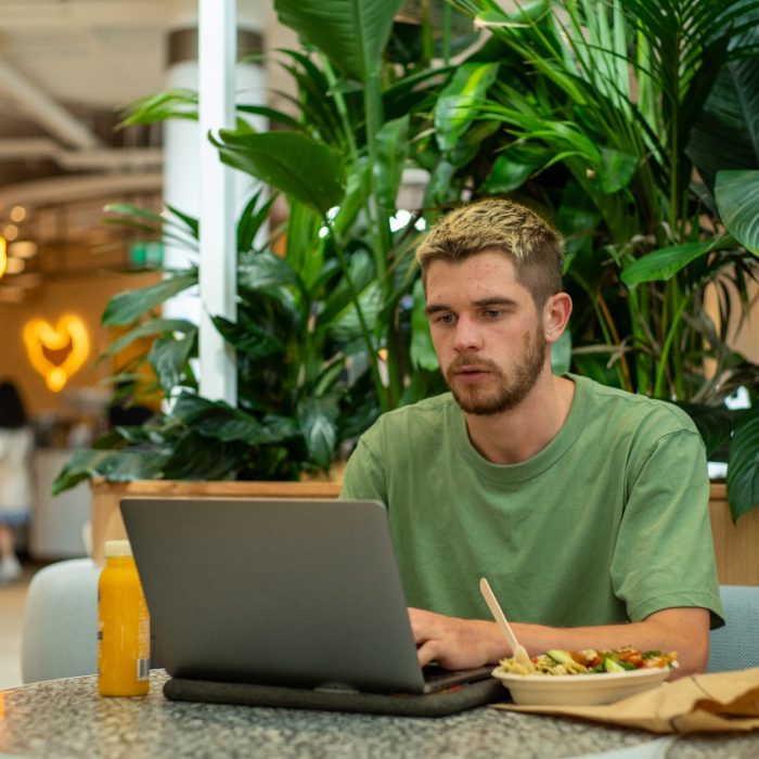 A student sitting at their laptop while eating lunch on Kensington Campus