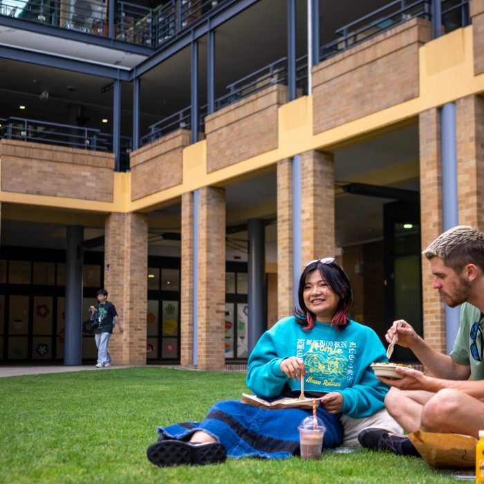 Two students chatting and eating on Helen Maguire Lawn on Kensington Campus