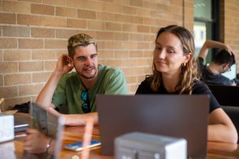 Students sitting at an outdoor table in the Quadrangle Building with their laptops