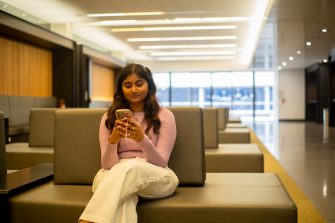 A student looking at their phone while sitting on a bench indoors on campus