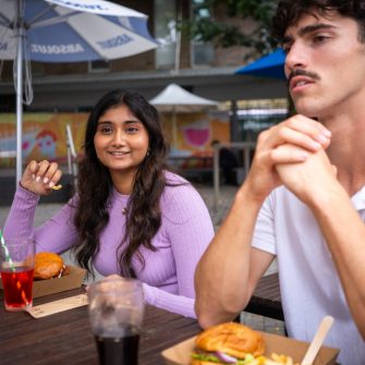 Students chatting while sitting at an outdoor table in The Roundhouse on Kensington Campus