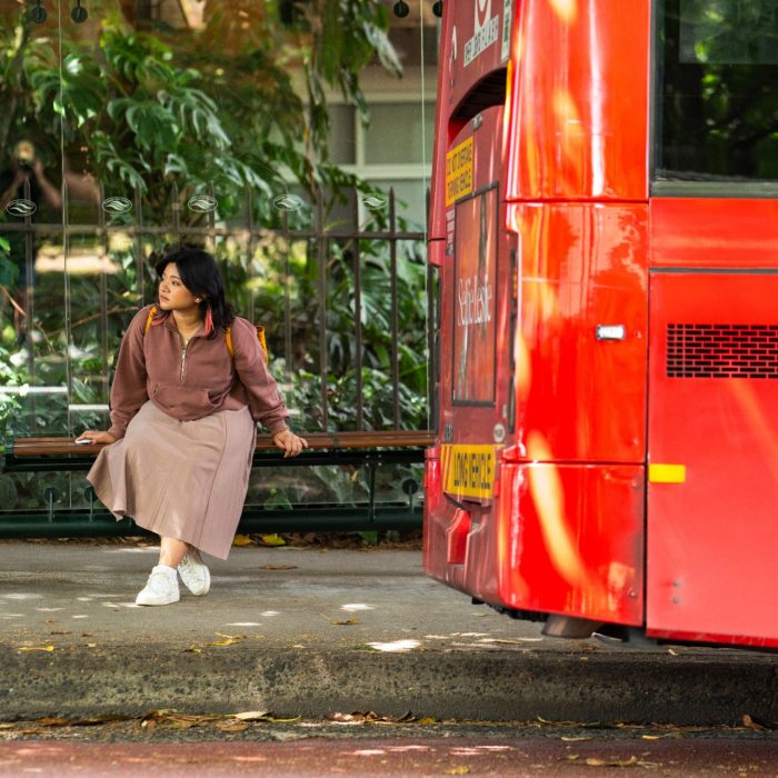 A student sitting at a bus stop on High Street outside Kensington Campus