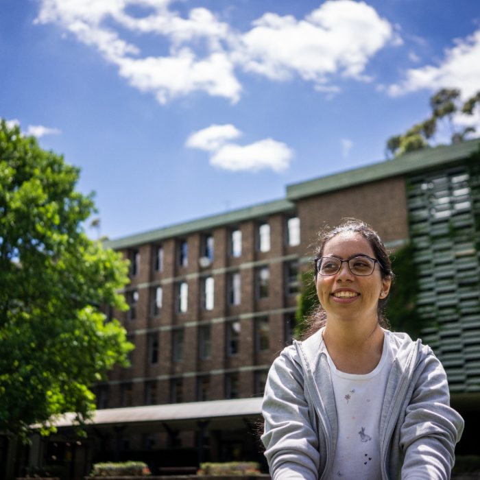 A student smiling while sitting on the grass on Library Lawn on Kensington Campus