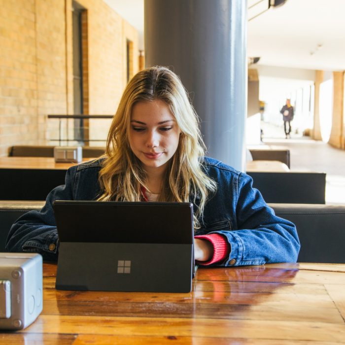 Students using their phones and laptops at the outdoor desks in the Quadrangle Building