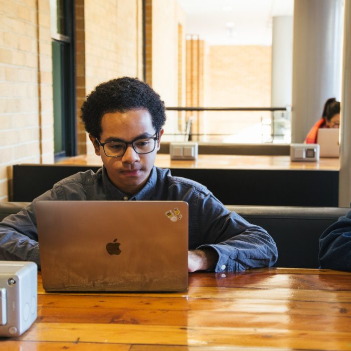 Students using their phones and laptops at the outdoor desks in the Quadrangle Building