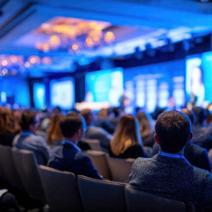 A crowd of people attends a business conference presentation in blue tones, showing corporate atmosphere and engagement Great for illustrating professional development topics.