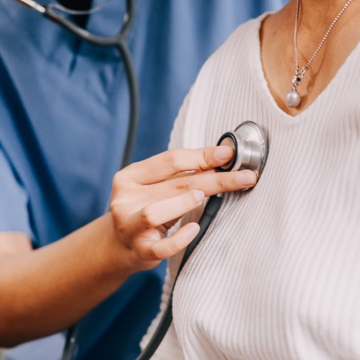 Lady coming to clinic for heart and lungs checkup, male doctor using stethoscope, listening to female patient's breath or heartbeat, sitting in clinic office