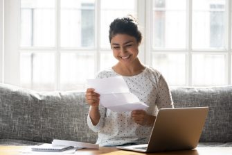 Woman sitting on couch at home reading paper notice receive good news feels happy, cheerful student female looking at document enjoy exam results or college admission letter concept