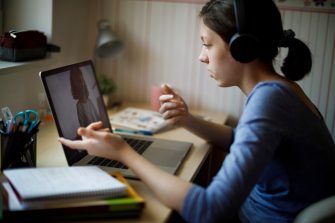 Teenage girl with headphones and laptop having online school class at home