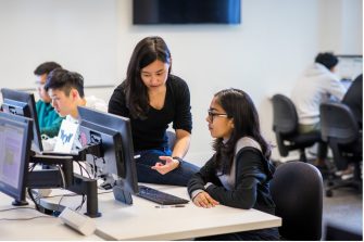 Two students engaging in conversation while working on a computer