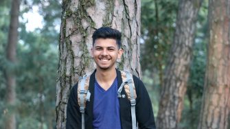 A man stands infront of a tree smiling