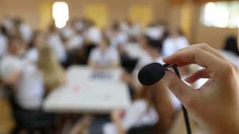 A hand holds a lectern microphone with the background blurred