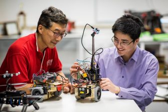 Engineering teacher and student working on electronic miniature vehicles in workshop