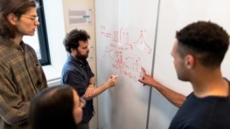 four Engineering students writing on and viewing whiteboard