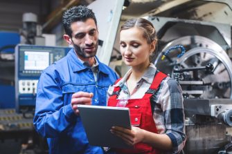 Woman and man manufacturing worker in discussion writing on tablet computer