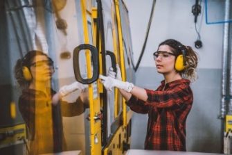 Female engineer in the lab with ear muffs, glasses and gloves closing yellow machine door