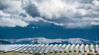 Big solar power plant with mountain ridge and dramatic clouds. Concept of environment protection and renewable energy generation to prevent climate change.