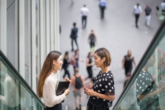 Two women smile and chat on an escalator in Sydney's CBD